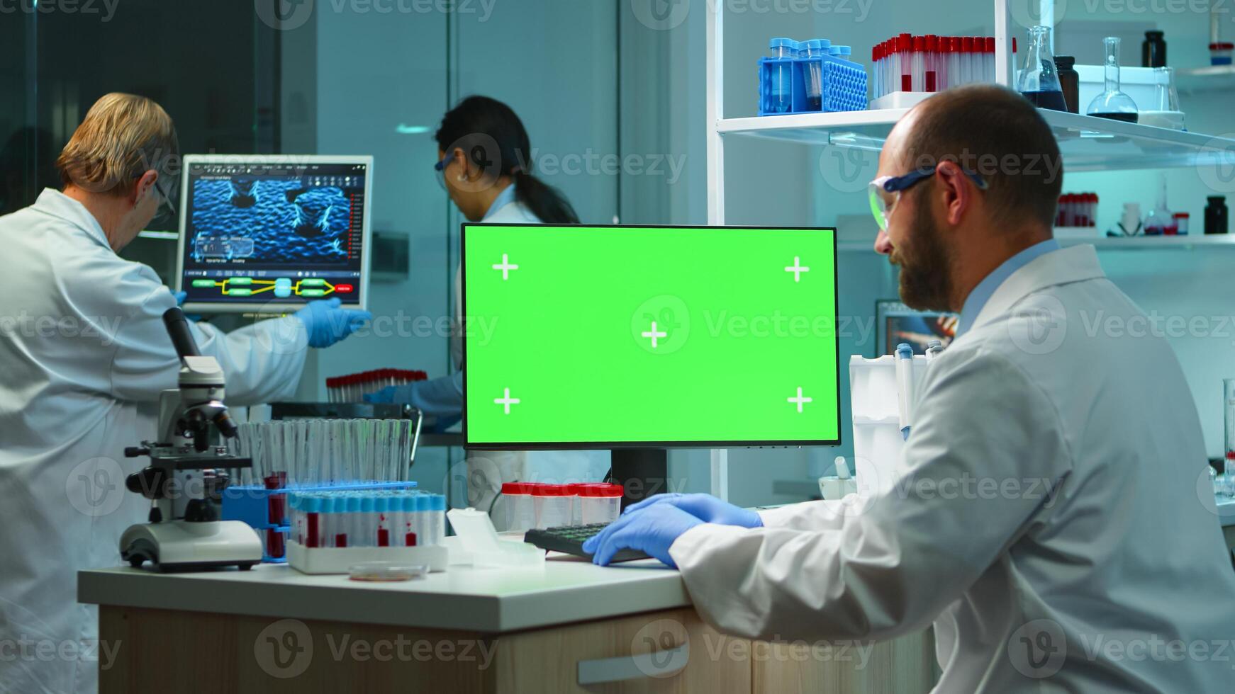 Man researcher looking at chroma key computer in modern equipped lab working overtime. Team of microbiologists doing vaccine research writing on device with green screen, isolated, mockup display. photo