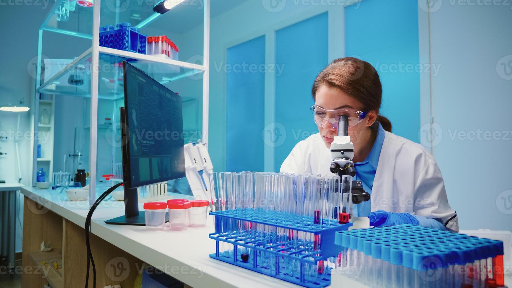 Team of scientist checking virus development using microscope analysing results at night in modern equipped lab. Group of chemists examining vaccine evolution using high tech for research. photo