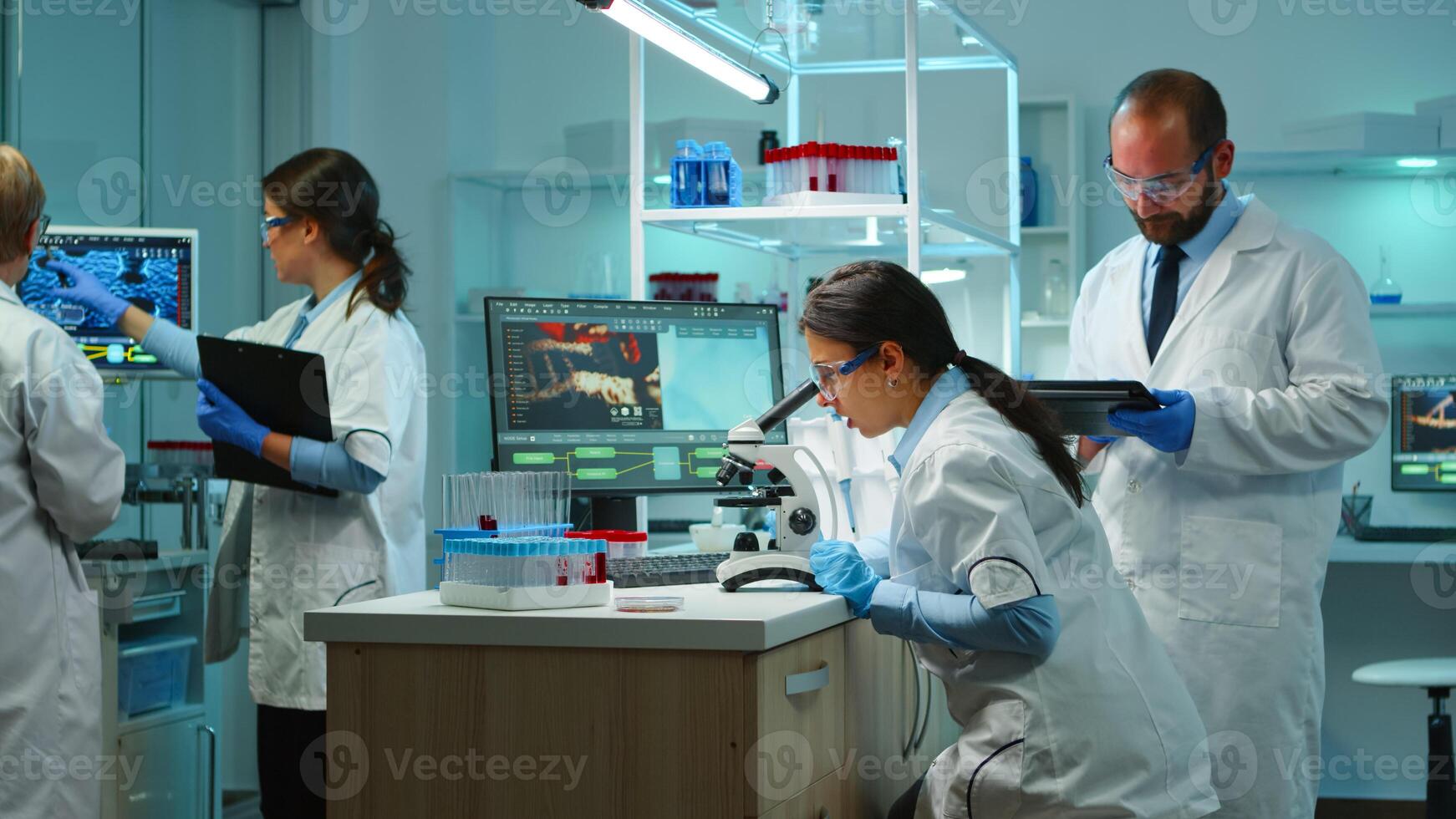 Team of biochemistry scientists developing drugs agains new virus, doctor checking samples while nurse taking noters on clipboard in modern equipped laboratory. Multiethnic scientists working photo