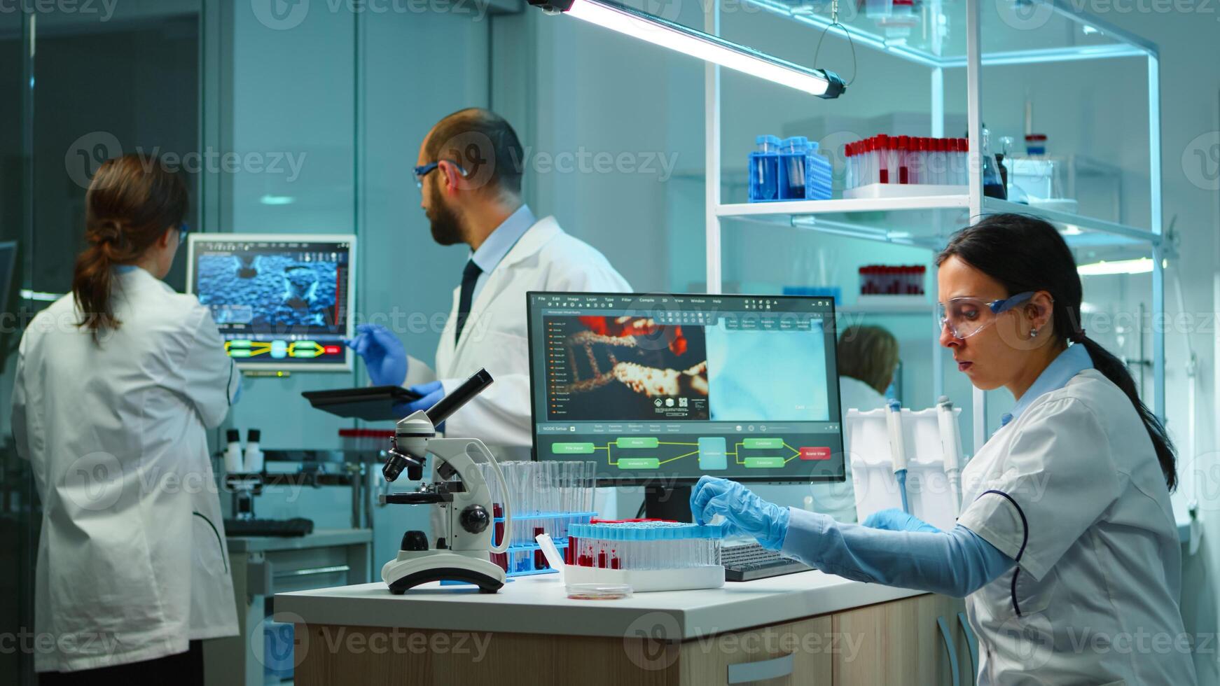 Scientist team checking virus development using high tech writing analysis results on computer in modern equipped lab at night. Doctors examining vaccine evolution with special tools for research. photo
