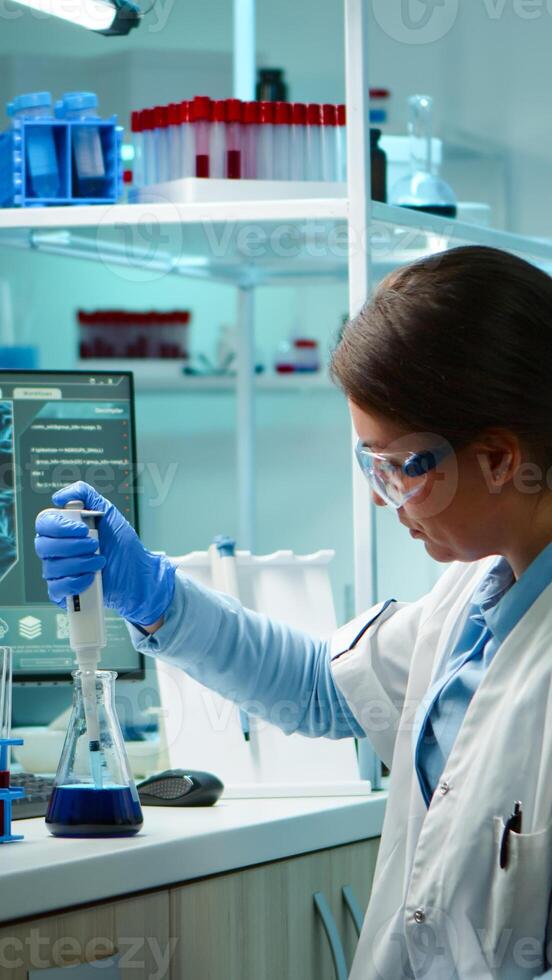 Scientist woman pipetting liquid to test tube late at night in modern equipped lab. Team examining virus evolution using high tech for scientific analysis of treatment development against covid19 photo