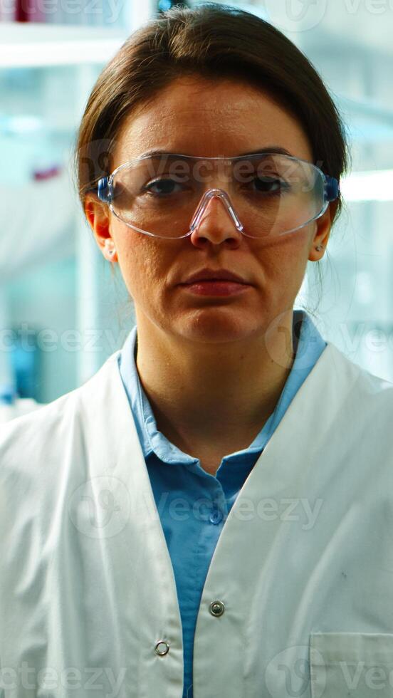 Close up of scientist nurse looking tired at camera sitting in modern equipped laboratory late at night. Team of specialists examining virus evolution using high tech for research, vaccine development photo