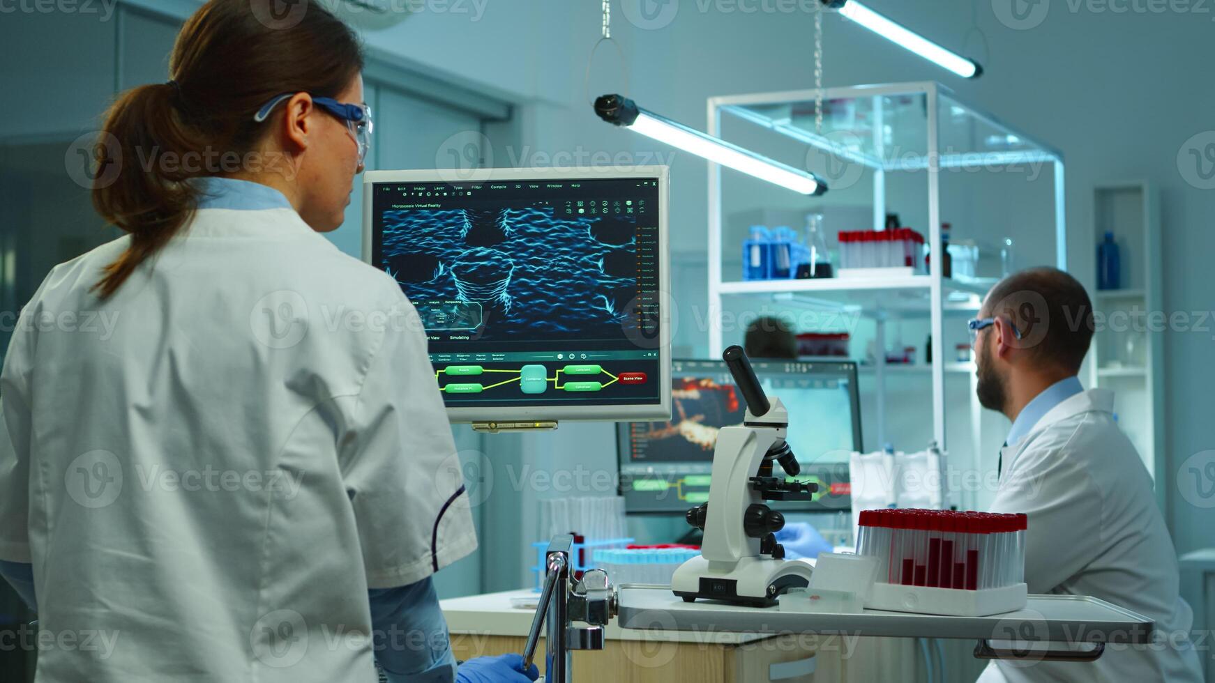 Team of medical research scientists conducting vaccine development with help of high tech, test tubes, micropipette and writing down analysis results on computer in modern equipped laboratory at night photo