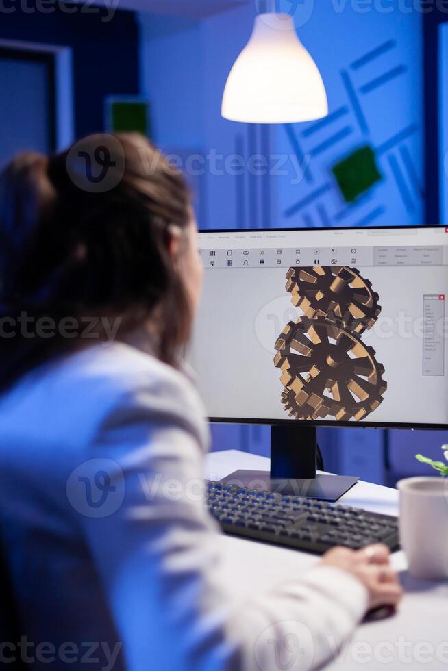 Focused architect working at new project using computer doing gear prototype late at night sitting at desk in start-up office. Industrial woman engineer studying on pc for development cad software photo