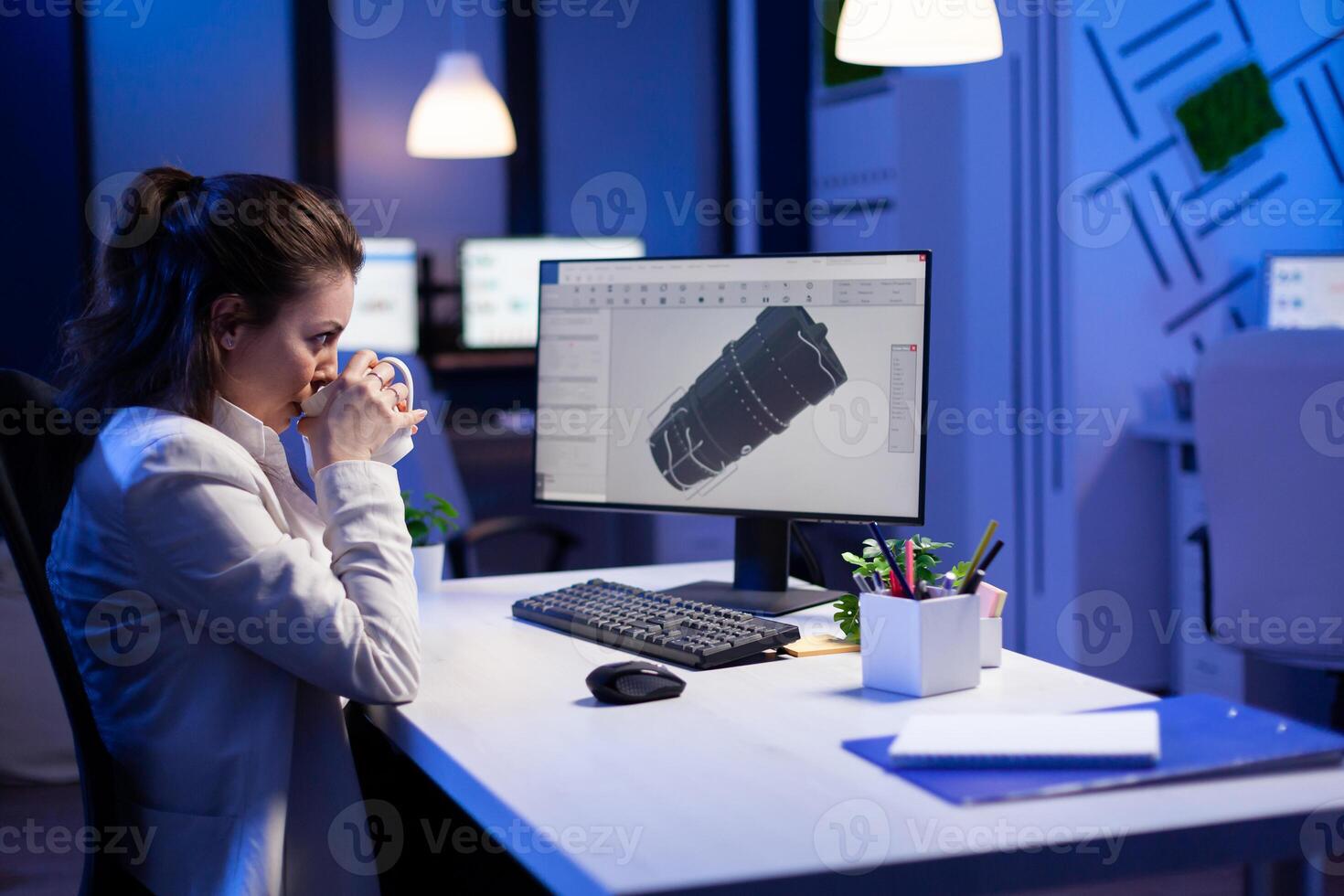 Woman engineer working late at night on 3D model of industrial turbine while drinking coffee in front of computer. Workaholic freelancer studying prototype design on pc showing cad software on device display photo
