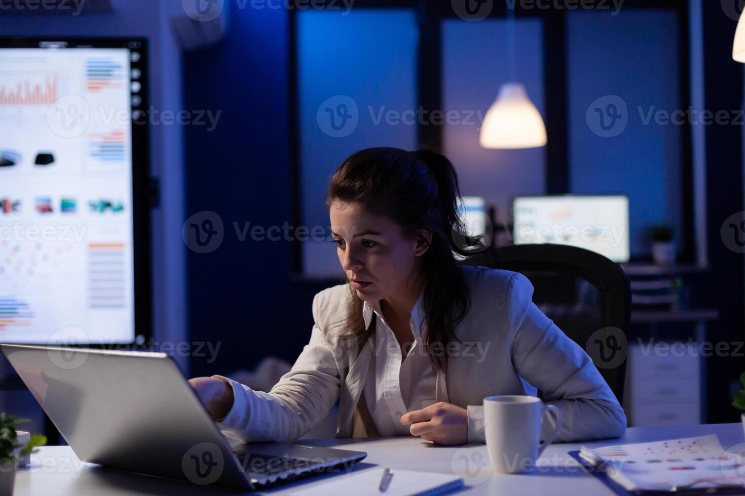 Stressed businesswoman checking profit resultes standing in business office late at night. Focused entrepreneur using technology network wireless for developing new marketing system photo