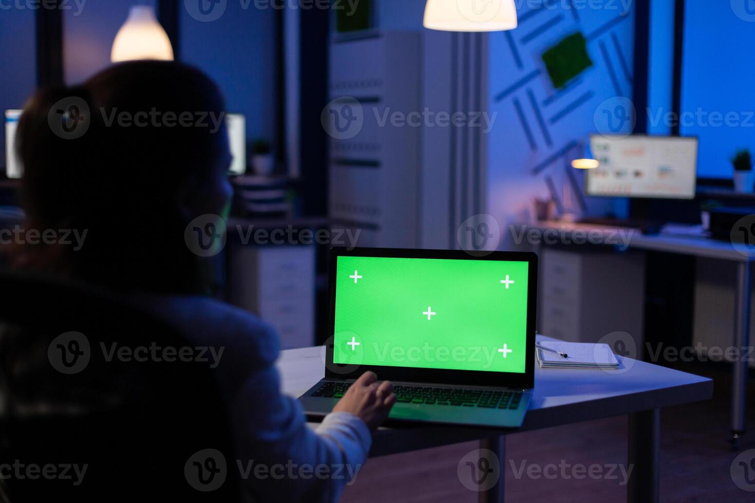 Back view of business woman looking at green screen laptop sitting at desk in start up company office . Exectutive manager watching desktop monitor display with green mockup, chroma key photo
