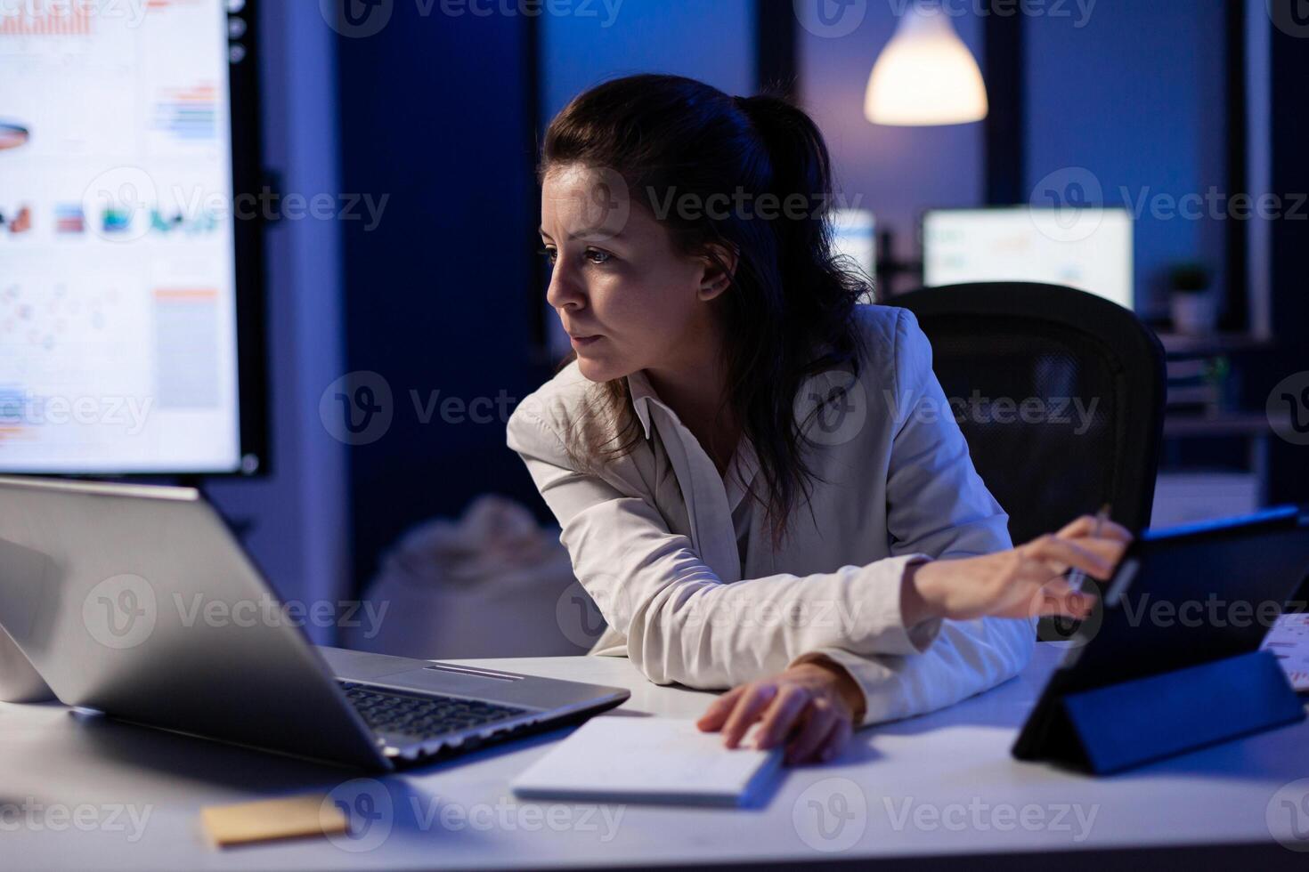 Manager woman using laptop and tablet in same time working on financial reports in business start-up office . Busy multitasking employee using modern technology network wireless late at night photo