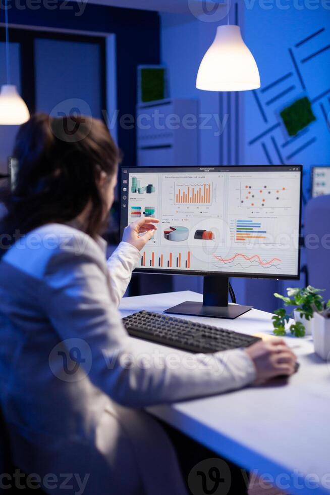 Back shot of overwhelmed woman working at night in front of computer, writing notes on notebook annual reports, checking financial deadline. Focused manager using technology network wireless photo