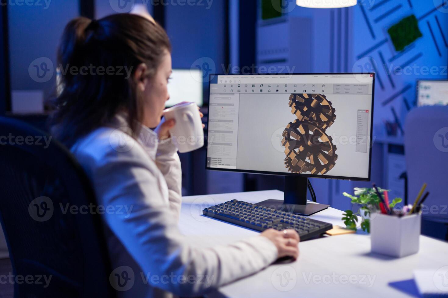 Focused architect working at new project using computer doing gear prototype late at night sitting at desk in start-up office. Industrial woman engineer studying on pc for development cad software photo