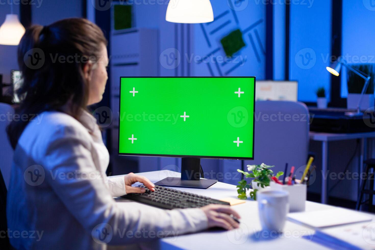 Businesswoman looking at green screen monitor of computer sitting at desk during online web conference. Freelancer watching desktop monitor display with green mockup, chroma key in business office photo