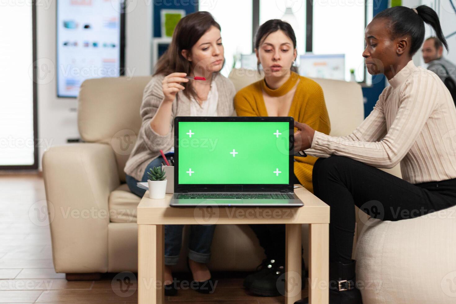 Laptop with green screen on table in start up company with multiethnic diverse coworkers working together behind it. African american woman discussing project strategy with colleques looking at tablet pc. photo