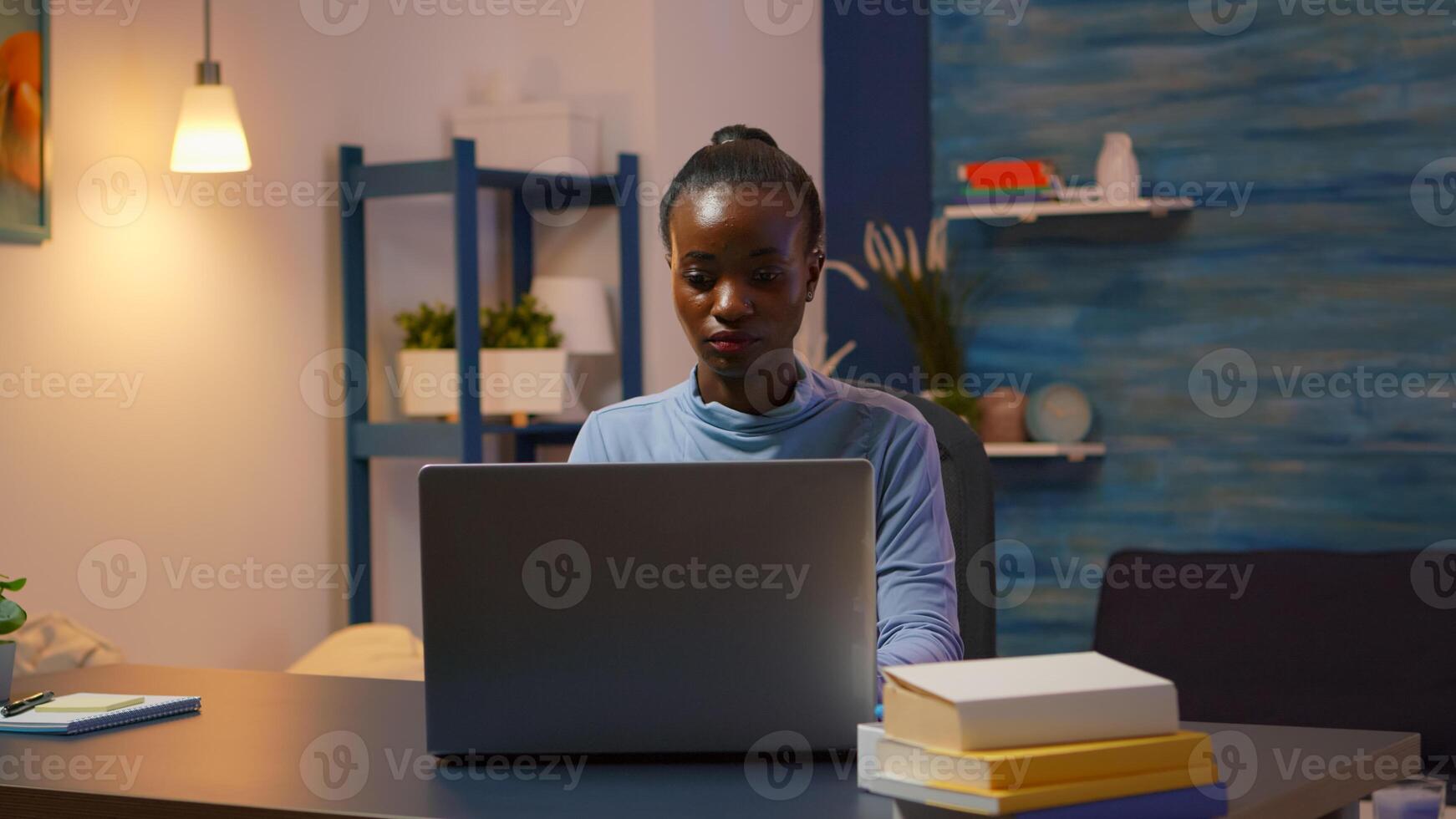 African woman coming in living room and typing on computer working from home overtime. Black entrepreneur sitting in personal workplace writing on keyboard looking at desktop respecting deadline. photo