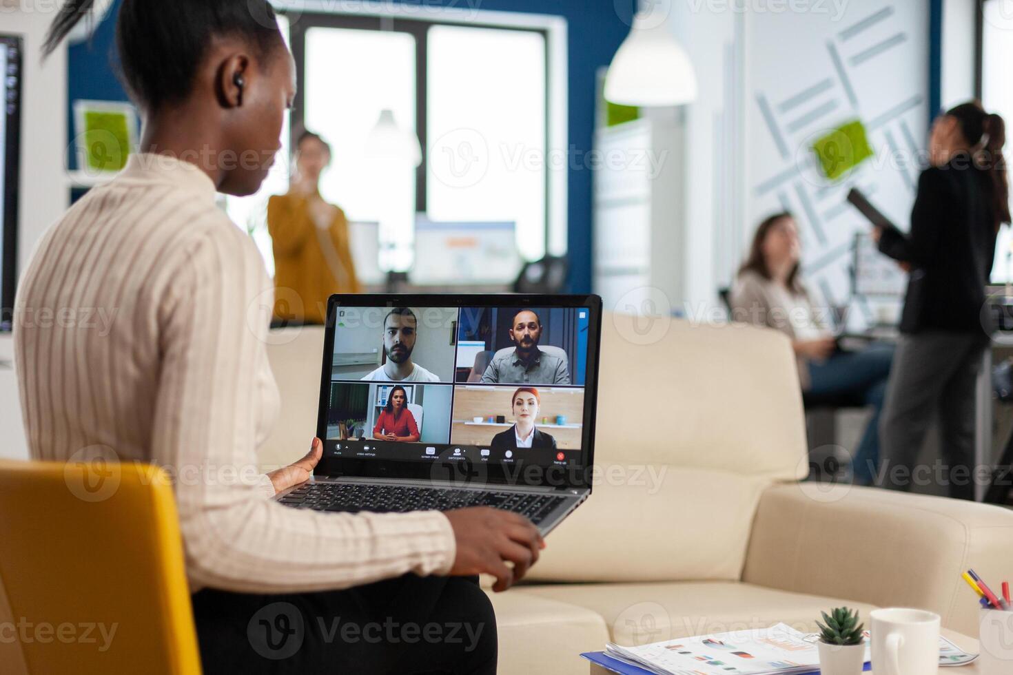 African manager woman discussing with remote colleagues using call holding laptop sitting on couch in business modern office. Diverse coworkers planning new financial project in modern company photo