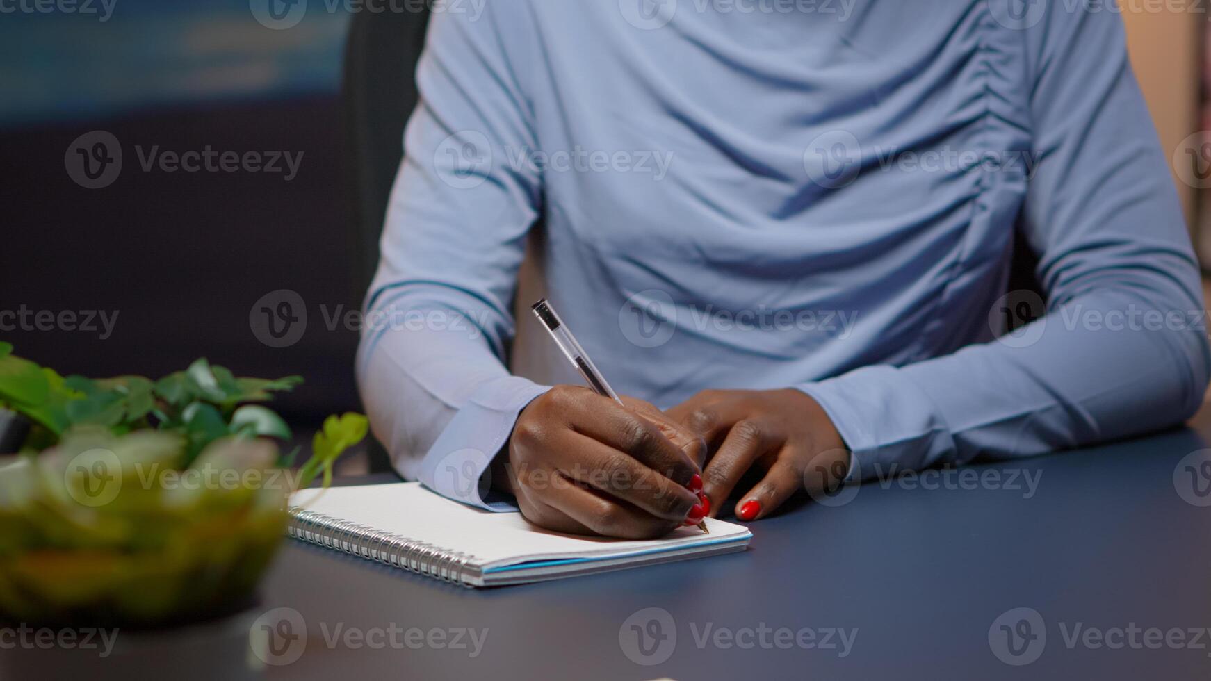 Close up of african businesswoman writing list of tasks for business project in notebook sitting at desk in living room working overtime. Black freelancer respecting deadline studying late at night photo