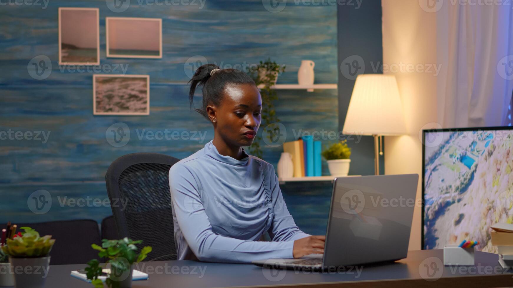 African young business woman coming at home workplace late night. Black entrepreneur working in moder living room overtime writing on keyboard looking at desktop respecting deadline of project. photo