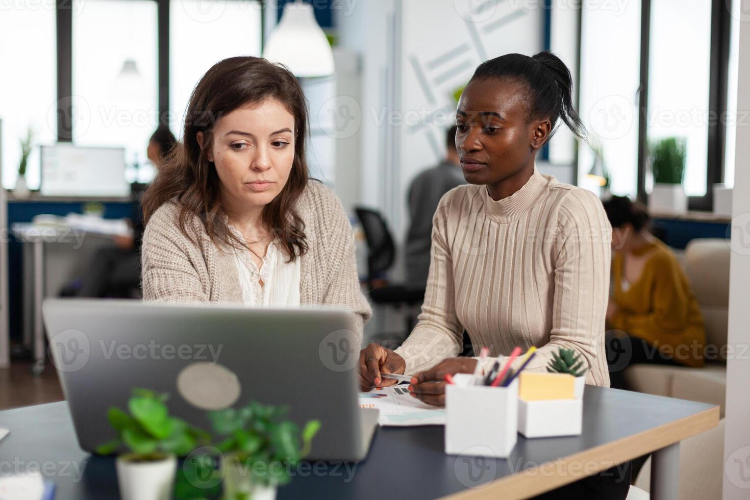 Startup diversity teamwork brainstorming sitting at desk in modern office, planning business strategy looking in laptop, searching management solutions. Multiethnic businesspeople working company photo