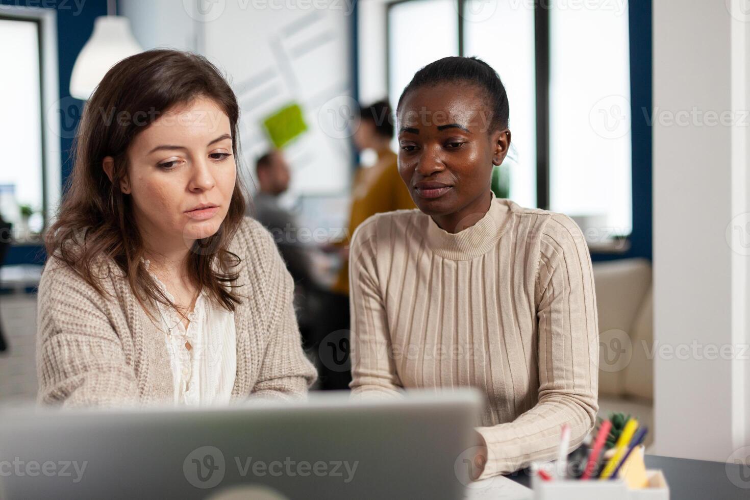 Startup diversity teamwork brainstorming sitting at desk in modern office, planning business strategy looking in laptop, searching management solutions. Multiethnic businesspeople working company photo