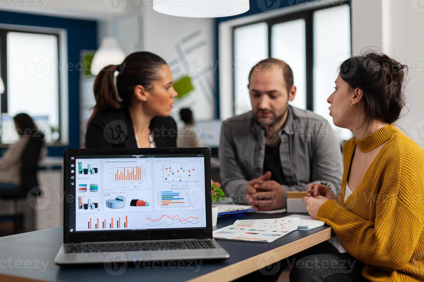 Business woman talking about financial project, taking notes, discussing start up ideas using laptop. Diverse employees gathered in co-working, working process in busy company, teamwork help concept photo