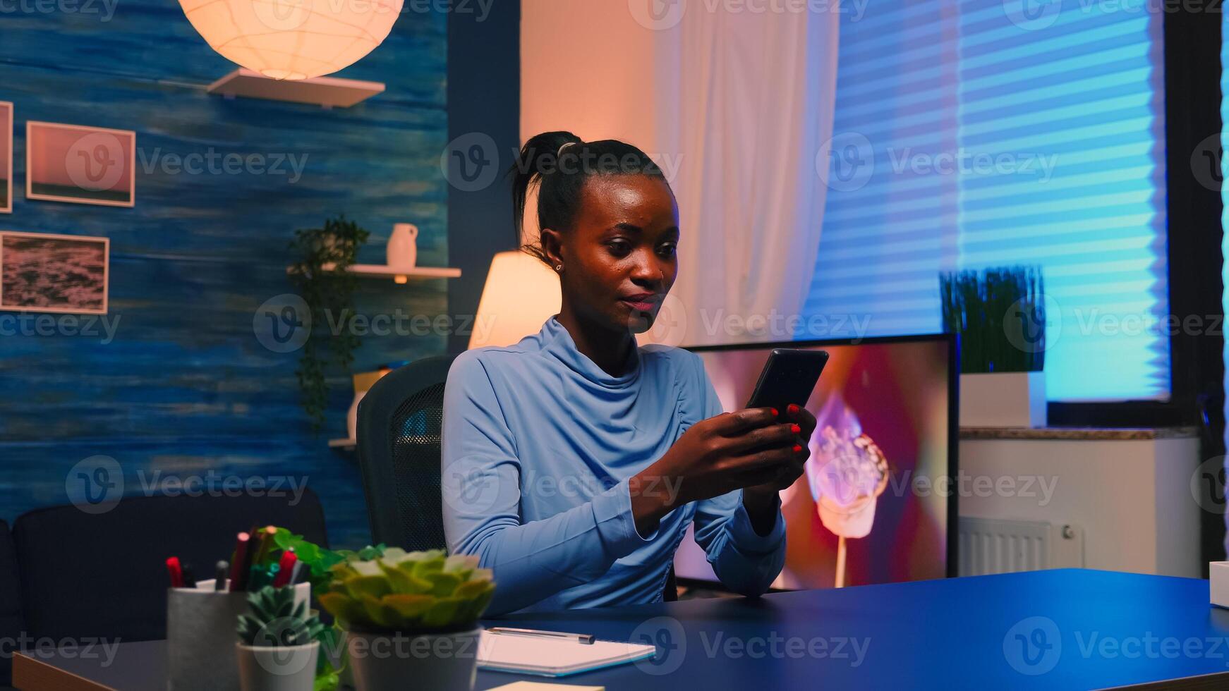 Black businesswoman browsing using smartphone sitting in living room office taking a break after hard work. African remote employee working overtime respecting deadline chatting with team. photo