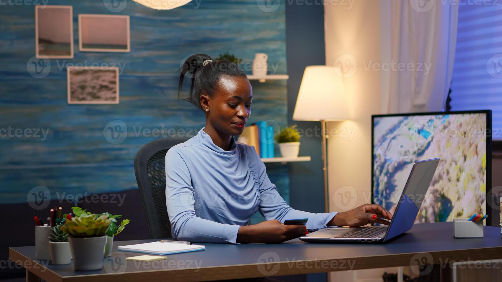 African american woman shopping online late at night sitting in living room with laptop using credit card. Employee making paymant transaction from home on digital notebook conected to internet photo