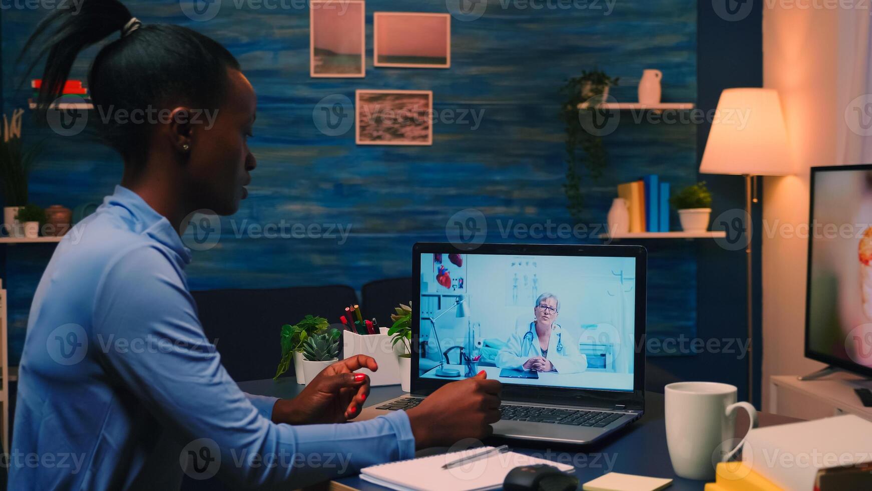 African lady writing notes during online medical consultation listening woman doctor sitting in front of laptop in living room. Woman discussing during conference about symptoms and treatment. photo