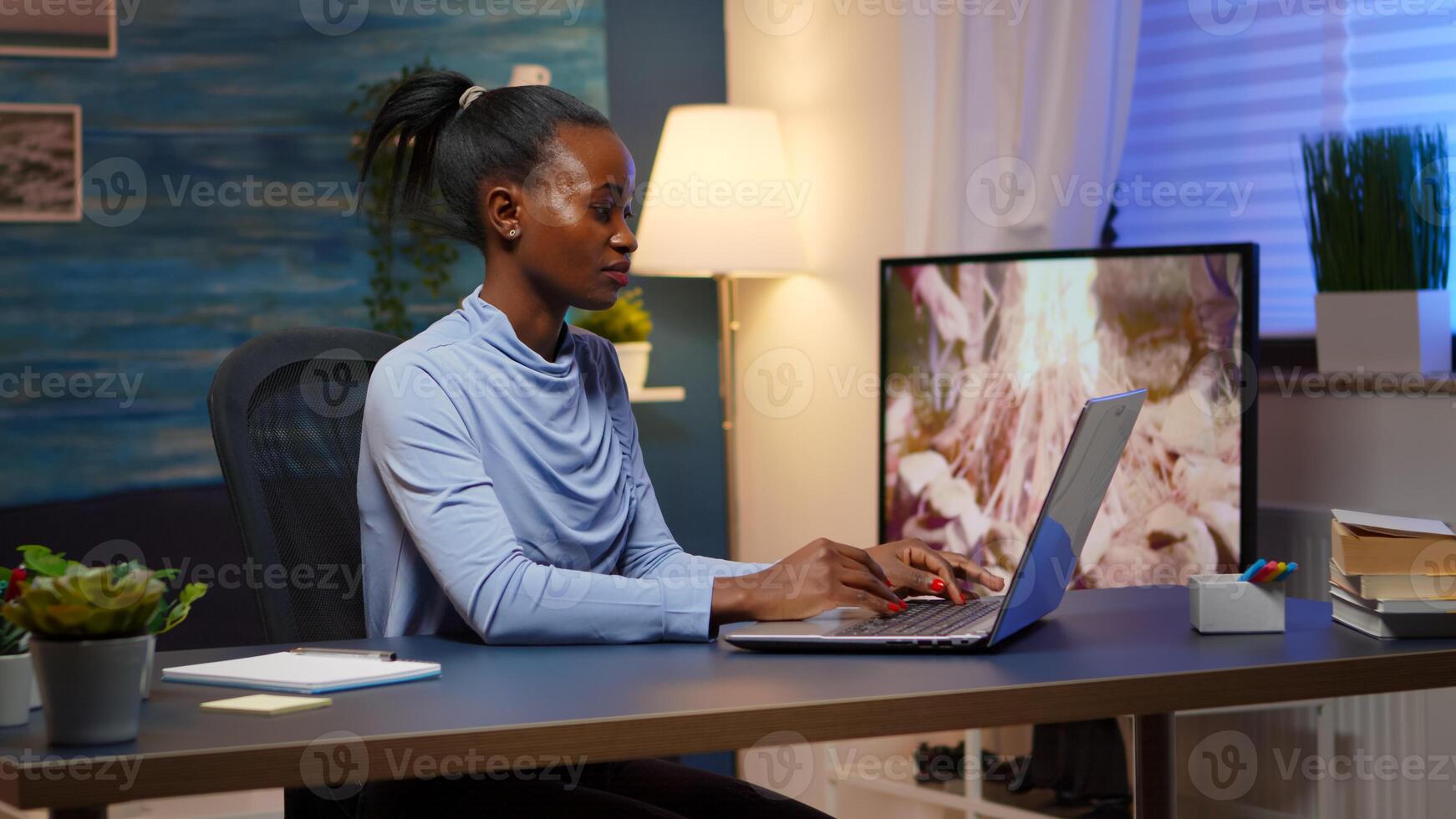 Overworked black entrepreneur working from home late at night on laptop. Tired focused employee using modern technology network wireless doing overtime for job reading writing, searching photo
