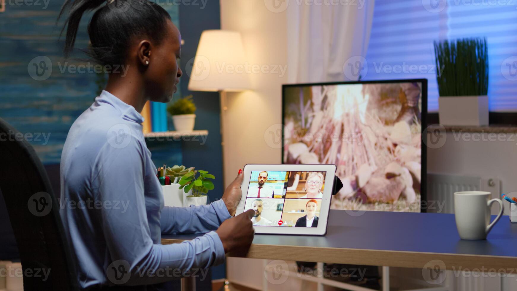 African business woman having webinar studying from home using internet technology on tablet in midnight. Lady using notebook with network wireless talking on virtual meeting at night doing overtime photo