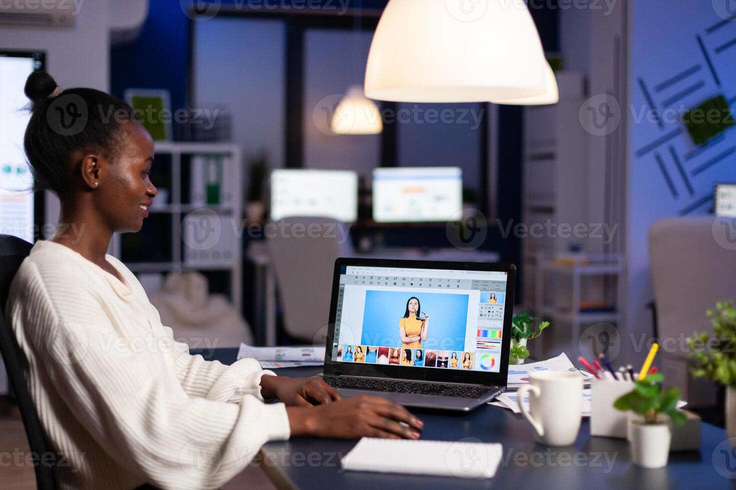 African professional woman photo retoucher working on laptop at new project in business office at night time. Content creator doing portrait retouching, artist, occupation, screen, graphic.