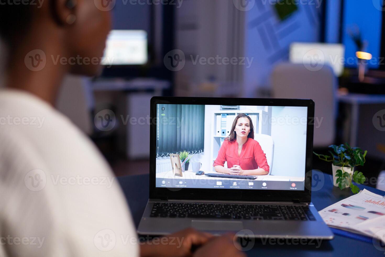 African businesswoman discussing remotely woman partner online sitting in front of laptop working in start-up office talking on call during virtual meeting at midnight, using headphone. photo