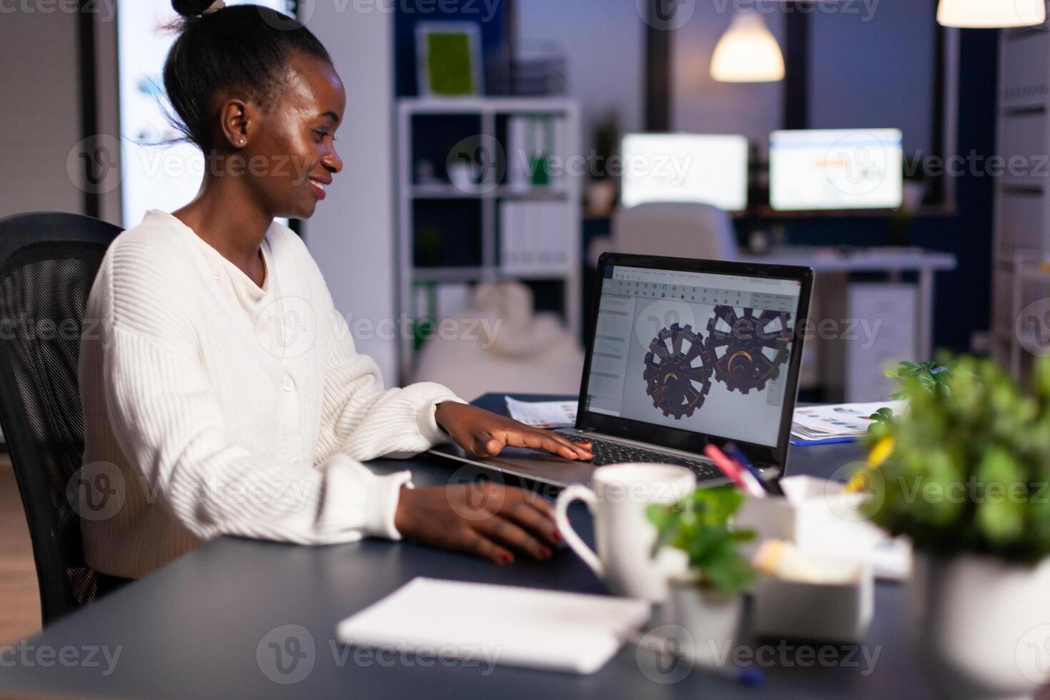 African mechanical designer working on computer late at night doing overtime to finish project. Freelancer studying prototype idea on pc showing cad software on device display. photo