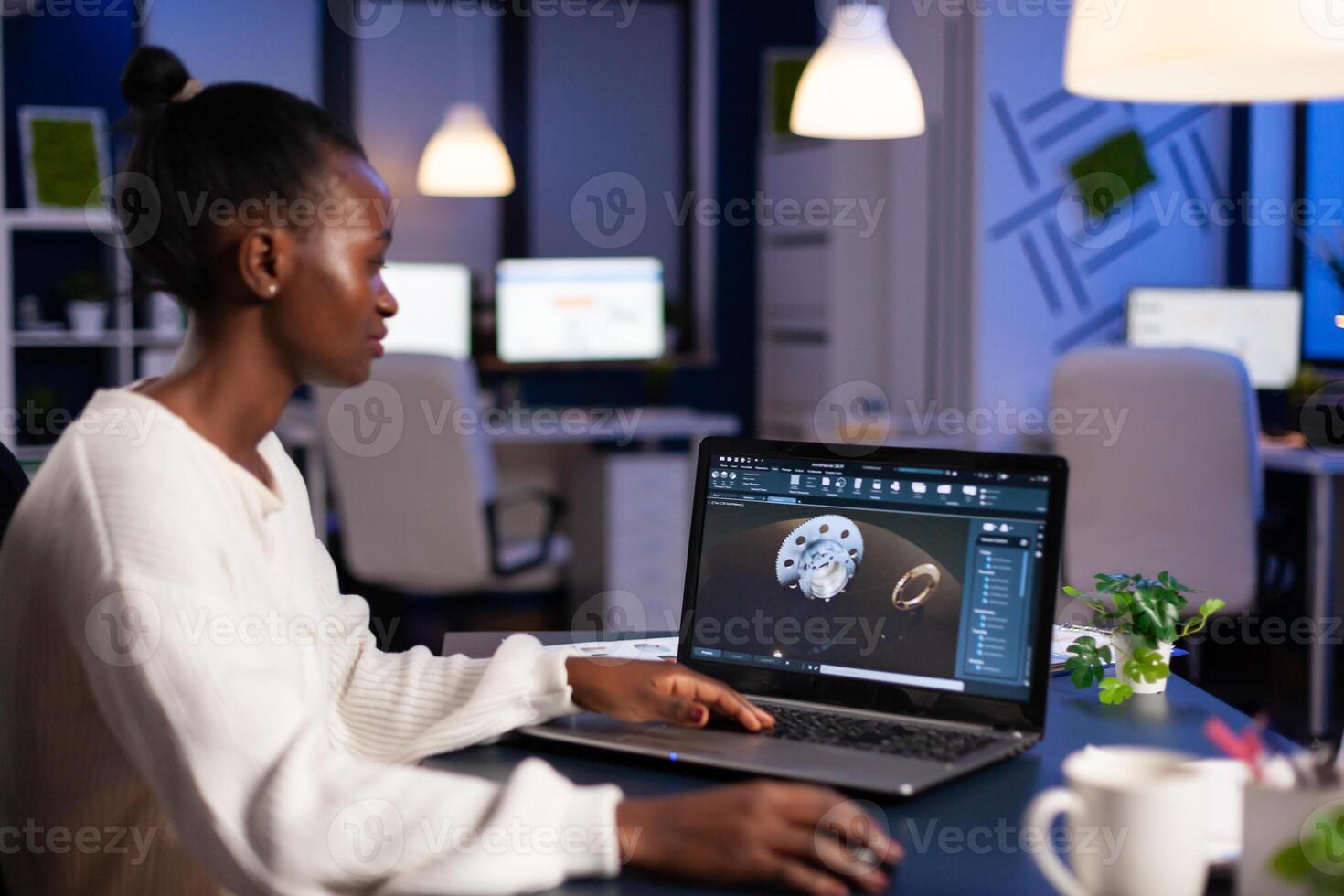 Black woman in mechanical industry working late at night doing overtime in start-up office. Industrial engineer studying prototype idea on pc showing cad software on device display. photo