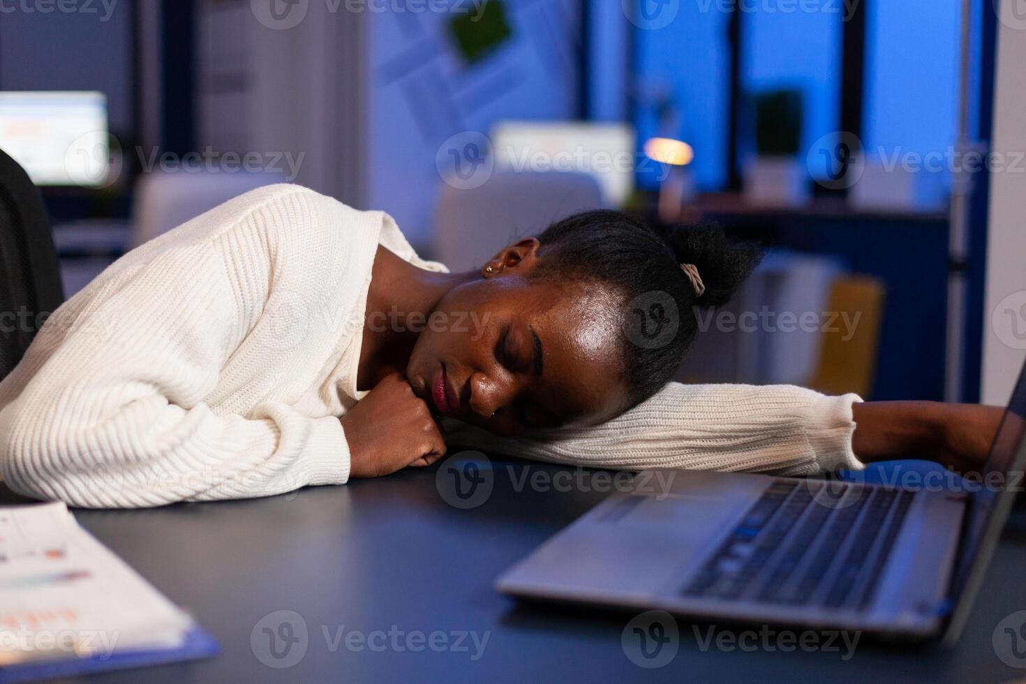 Tired exhausted african american businesswoman sleeping on desk table late at night in startup office after working at management statistics. Workaholic black manager planning company strategy photo