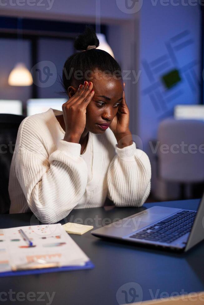 Exhausted african american businesswoman massage forehead having headache pain suffering from migraine. workaholic Tired black entrepreneur working at company strategy late at night in office photo