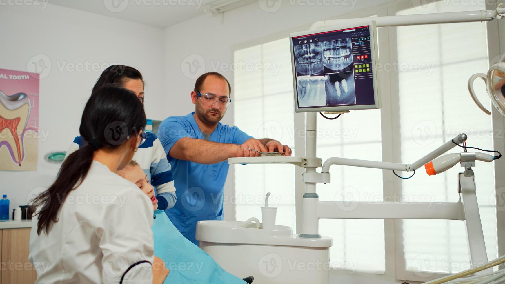 Pediatric dentist showing on monitor teeth x-ray reviewing it with mother and daughter. Doctor and nurse working together in modern stomatological clinic, explaining to old woman radiography of tooth photo