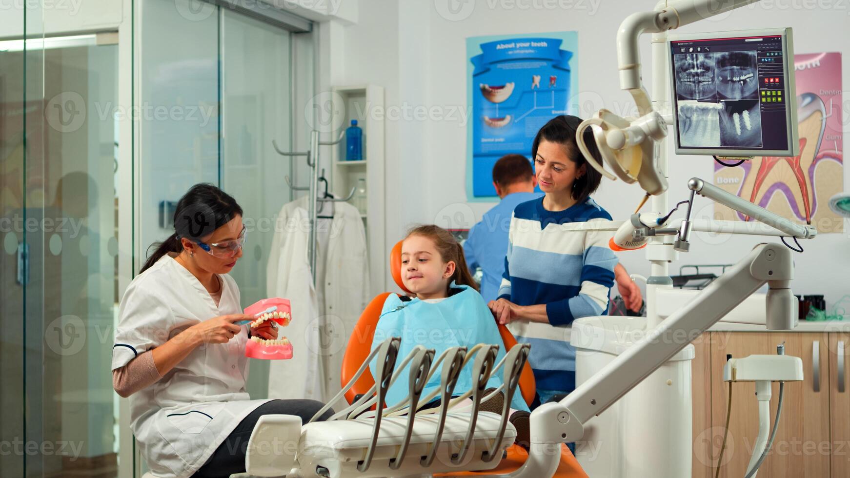 Stomatologist holding plaster model of the mandible speaking with girl patient. Dentist showing the correct dental hygiene using mock-up of skeleton of teeth, sample of human jaw with toothbrush photo
