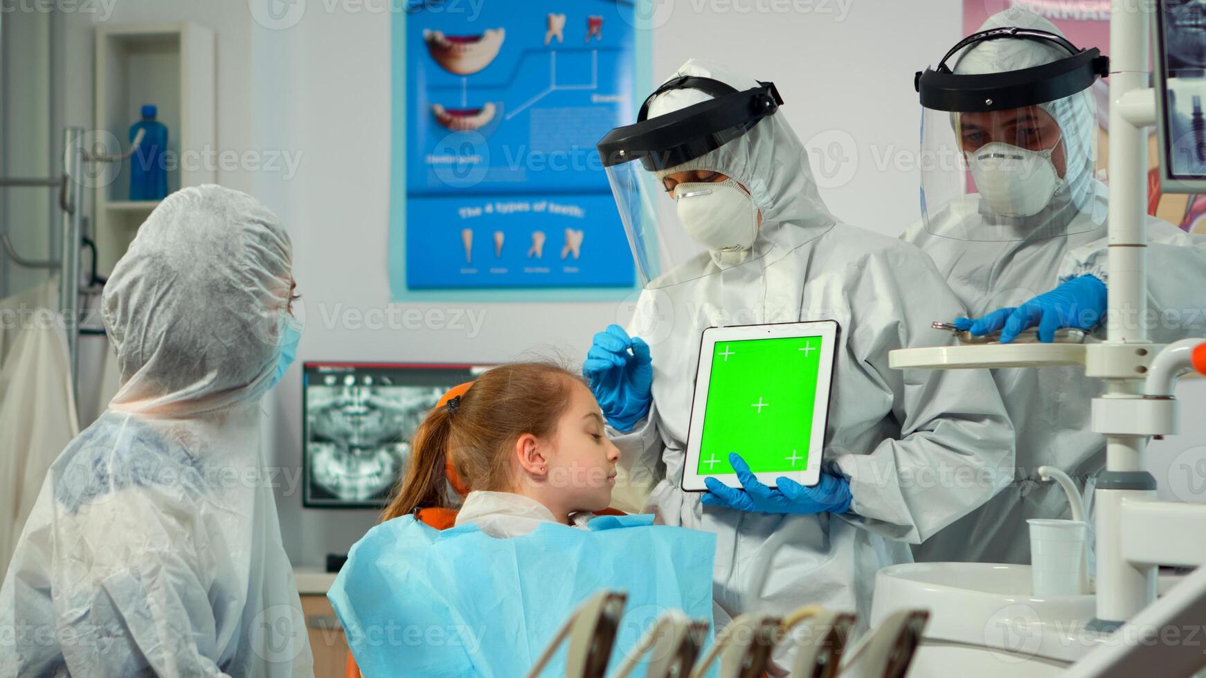 Dentist with face shield pointing at green screen display talking to child with toothache during coronavirus epidemic. Explaining using monitor with chroma key izolated chroma pc key mockup display photo