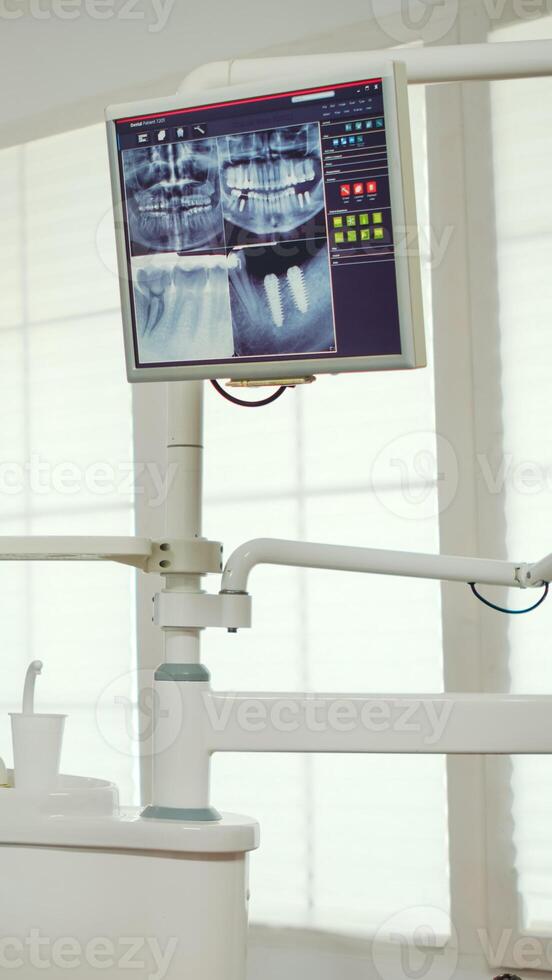 Pediatric dentist showing on monitor teeth x-ray reviewing it with mother and daughter. Doctor and nurse working together in modern stomatological clinic, explaining to old woman radiography of tooth photo