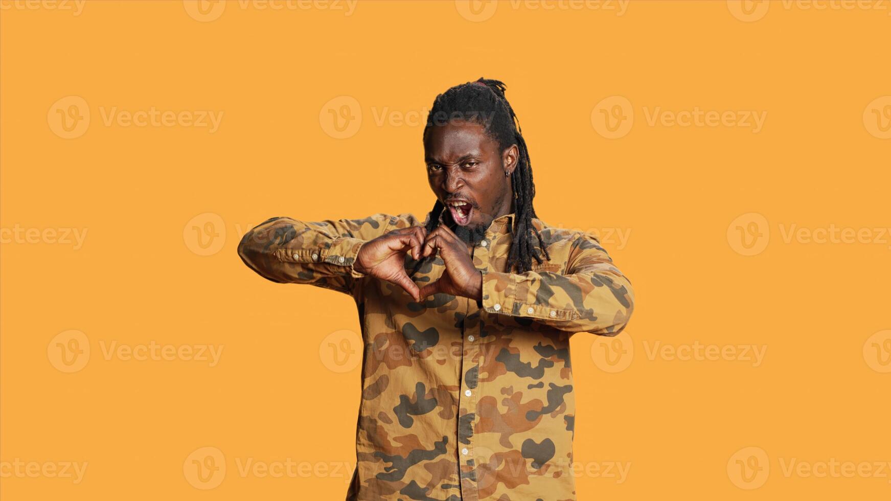 Male model presenting heart shape sign in studio, creating romantic flirty gesture to show his sincere emotions and feelings. Young adult doing love symbol on camera, romance concept. photo