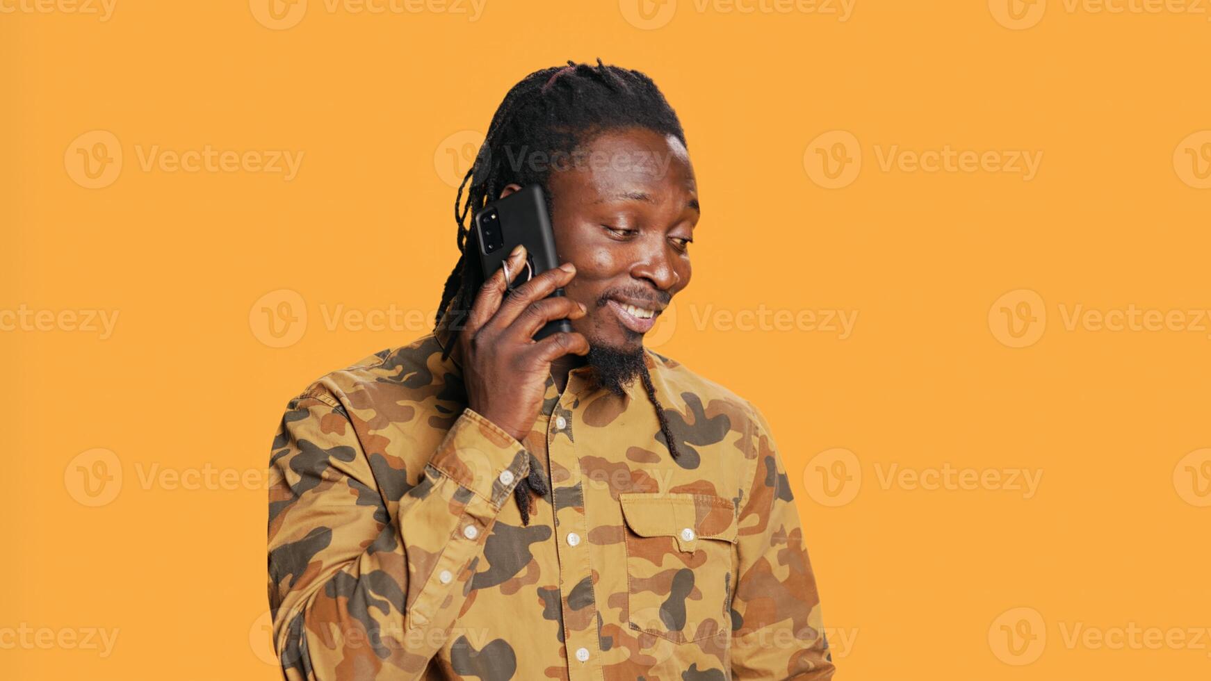 Cool person with braids answering phone call on camera, talking to friends or family in studio. African american trendy man chatting remotely with people, telephone line over background. photo