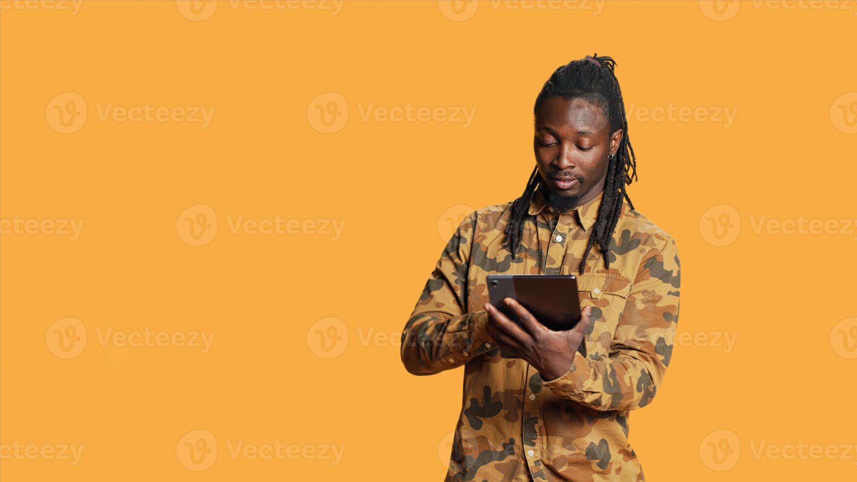 Modern person navigating online on tablet in studio, using mobile device to check social media apps and browse internet pages. African american man checking websites on gadget. photo