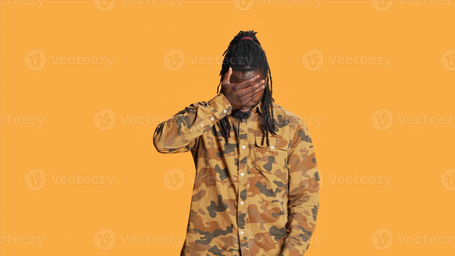 African american guy shows three wise monkeys sign standing over orange background, presenting symbol to not see, hear or speak. Serious person covering his mouth, eyes and ears on camera. photo