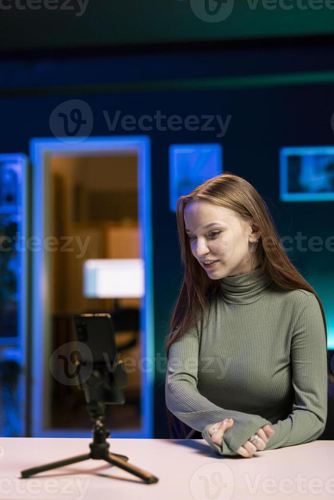 Smiling gen Z content creator utilizes smartphone on tripod to shoot introductory segment for vlog channel. Teenage internet star welcomes devoted fan community, introducing today subject photo
