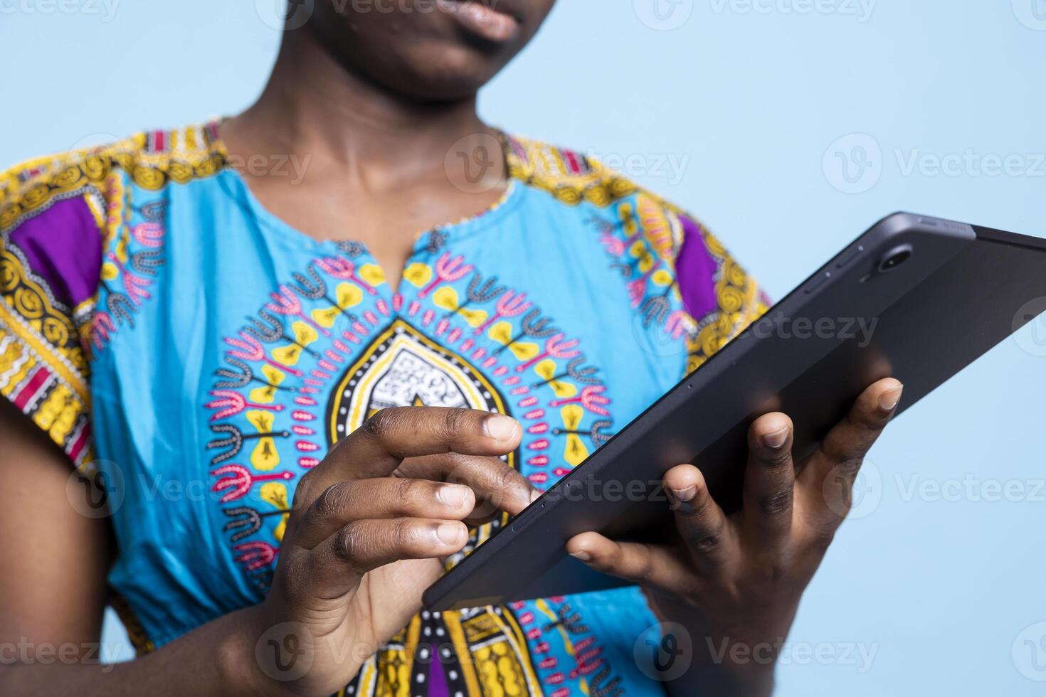 Female model of African American descent uses tablet to browse social networks and read articles from internet sources. Young woman in vintage traditional clothes searches web pages. photo