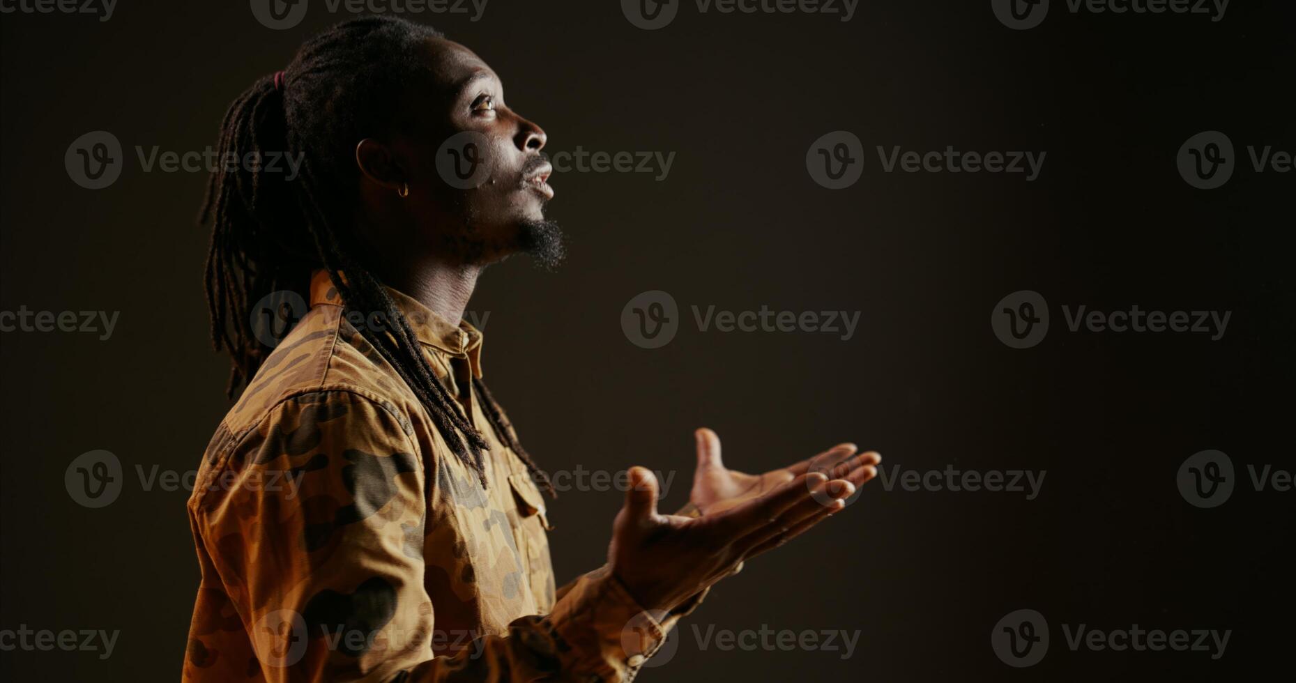 Spiritual person believing in God and praying on camera, showing belief and being hopeful over black background. Religious adult feeling optimistic and talking to Jesus. Handheld shot. Close up. photo