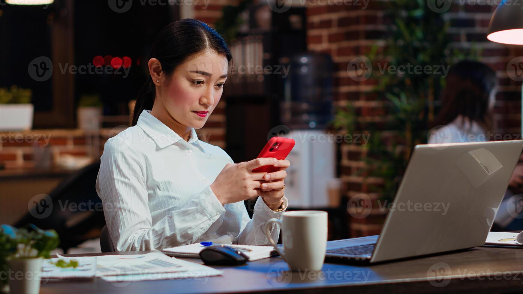 Smiling employee at work texting friends on cellphone, taking break from solving project tasks. Relaxed businesswoman using mobile phone to unwind in office late at night photo