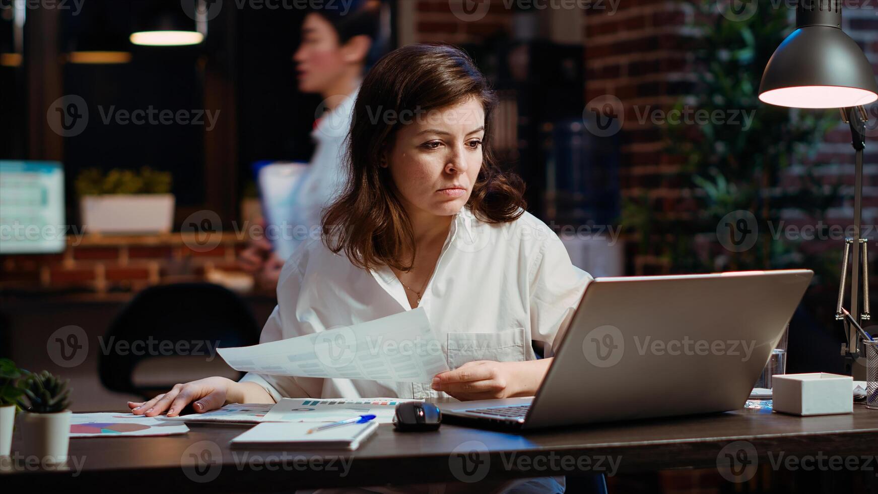 Worker looking over paperwork containing financial graphs, researching key data for company project. Businesswoman looking over accounting figures and charts on papers late at night at desk photo
