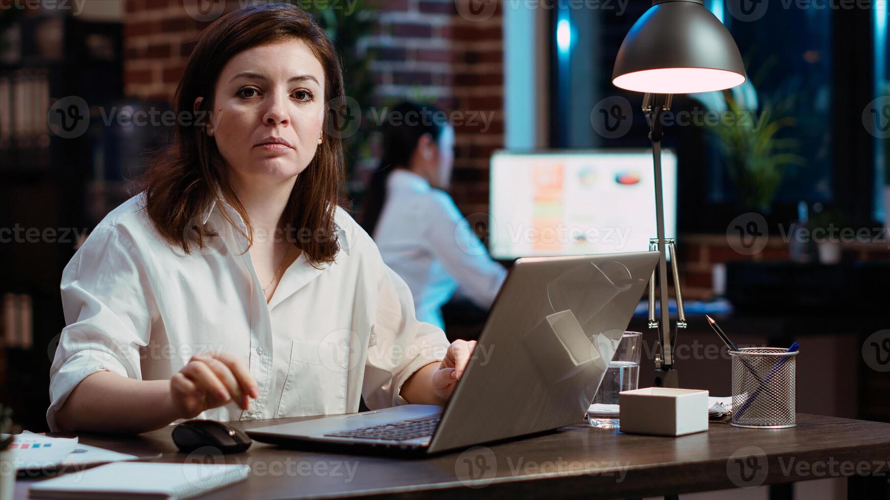 Portrait of smiling businesswoman planning marketing project on laptop late at night. Cheerful office worker working nightshift, making strategy research to create financial development, camera B photo