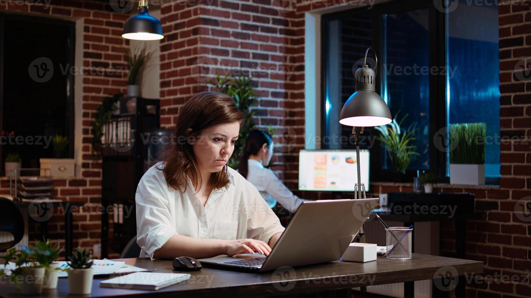 Businesswoman working overtime for company project, doing tasks in office overnight. Employee looking over accounting figures on laptop screen late at night, inputting data photo