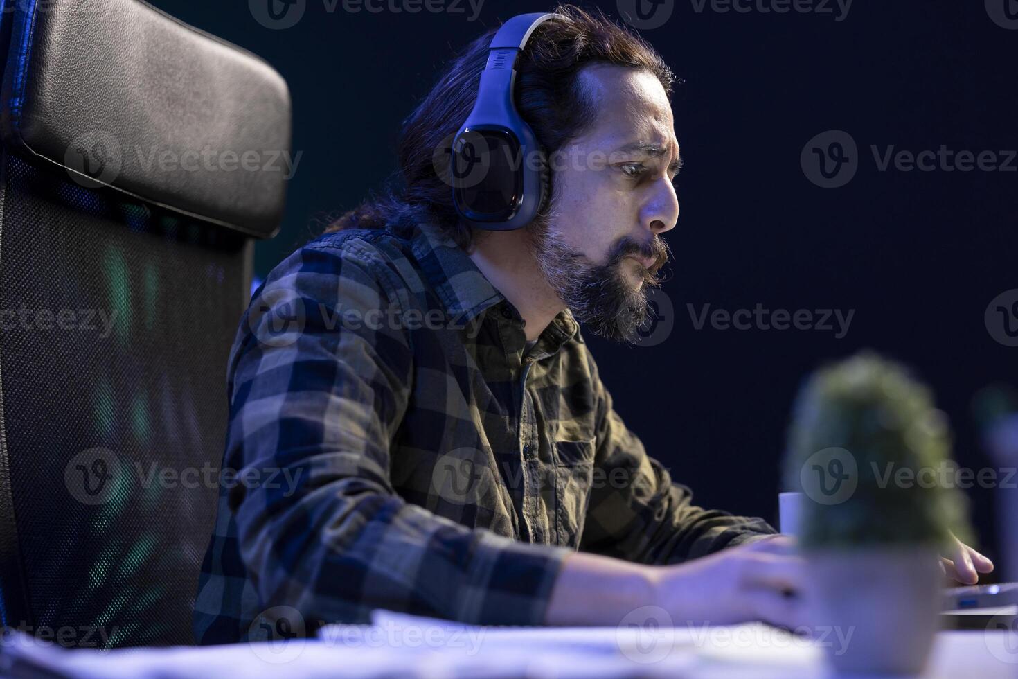 Focused man brings his laptop to virtual meetings and surfs the internet with wireless headphones on. Bearded guy who multitasks by watching movies and doing online homework. photo